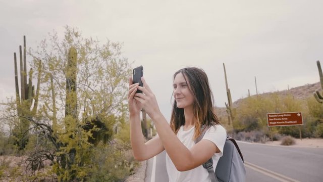 Slow motion young happy smiling traveler woman taking smartphone photo of cactus desert during national park excursion.