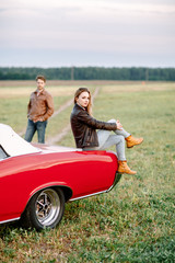 The girl with the leather jacket and on the trunk of the car. Сountryside.