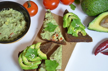 A delicious Bowl of Guacamole next to fresh ingredients on a table with tortilla chips and salsa....