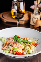 Concept of Italian cuisine. Caesar salad with salmon, lettuce mix, cherry and parmesan cheese. A glass of white wine on the table. Serving dishes in the restaurant. copy space