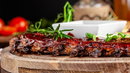 Grilled ribs with potatoes in a rustic style with barbecue sauce. Serving dishes in the restaurant on a wooden board. A glass of cool wine. Background image close up. copy space
