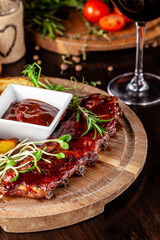 Grilled ribs with potatoes in a rustic style with barbecue sauce. Serving dishes in the restaurant on a wooden board. A glass of cool wine. Background image close up. copy space