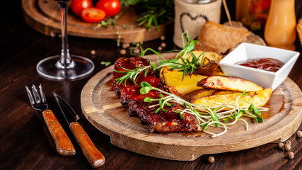 Grilled ribs with potatoes in a rustic style with barbecue sauce. Serving dishes in the restaurant on a wooden board. A glass of cool wine. Background image close up. copy space