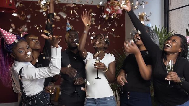 Six african friends with glass of champanage on the birthday party throwing golden confetti, jumping and dancing.