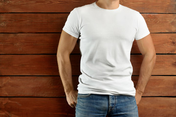 Athletic fit guy in a blank T-shirt and blue jeans on a brown wooden studio background.