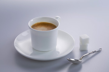 Studio shot of a cup of expresso coffee with sugar lumps and a silver spoon.