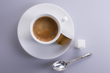 Cup of expresso coffee seen from above with sugar lumps, a silver spoon and a coffee capsule.