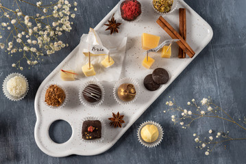 Set of fine chocolate candies and cheese. White, dark and milk chocolate, brie, blue cheese, goat cheese and parmisan on the plate. Chocolate cheese plate, top view.
