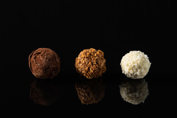 Fine chocolate candies on black background with reflection. White, milk and bitter dark chocolate.