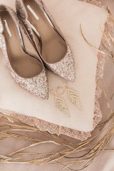 Blush pink bridal shoes and accenting jewelry with gold floral decoration. Pink background. Close up and top view. 