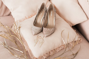 Blush pink bridal shoes and accenting jewelry with gold floral decoration. Pink background. Close...