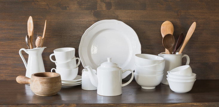 Crockery, clayware, white utensils and other different stuff on wooden tabletop. Kitchen still life.