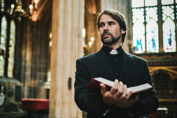 Christian priest standing by the altar - obrazy, fototapety, plakaty