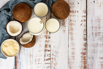 Coconut, glass of coconut milk and bowl with coconut flakes on a white wooden background. Top view. With copy space