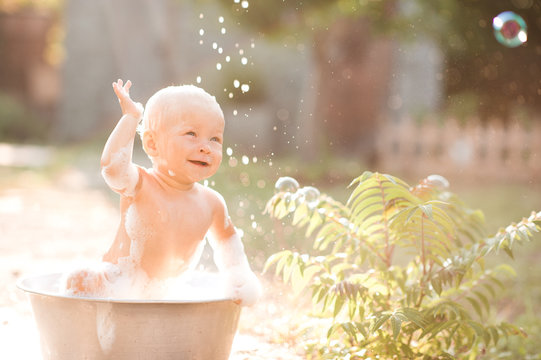 Happy Baby Taking Bath In Bathtub With Soap Bubbles Outdoors. Happiness. Childhood.