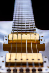 A very close view of an electric rock guitar body, strings and pickups
