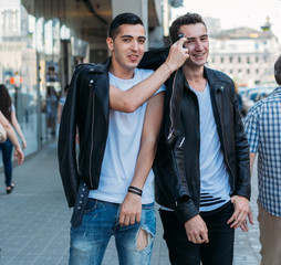 beautiful and attractive guy is standing in the city, posing. near the mirror building. walk around the city in black glasses. communication. meeting friends.