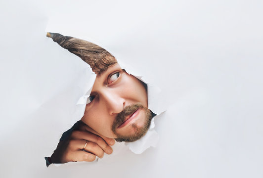 Portrait of a man looking through the hole in white paper. Distrustful look. Man's curiosity and gossip. A jealous husband.