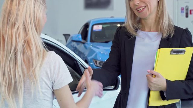 Female customer receiving car keys, shaking hands with saleswoman. Cropped shot of a professional car dealer handing keys to client, selling an automobile. Contract, agreement concept
