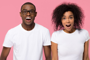 Amazed african couple feeling excited on pink studio background
