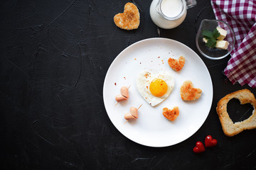 Morning breakfast on Valentine's Day. Fried eggs,sausage and toasts in the shape of a heart, milk,butter and fresh greens.Top view.Valentine's Day concept.