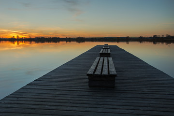 Long wooden bridge with benches and a sunset over the tranquil lake