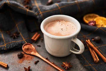 Hot cocoa drink in retro mug with ingredients: cinnamon, orange, anis and cove on black concrete table. Winter drink. Copy space for text.