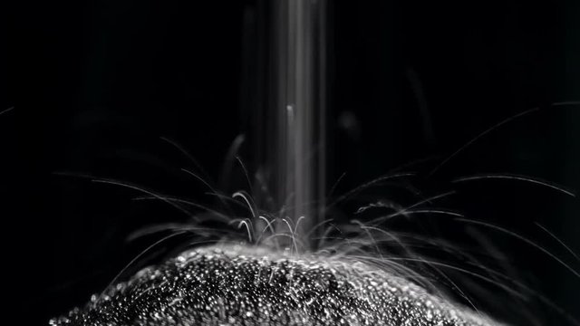 Dark sand is poured into the lower part of the hourglass with a thin trickle