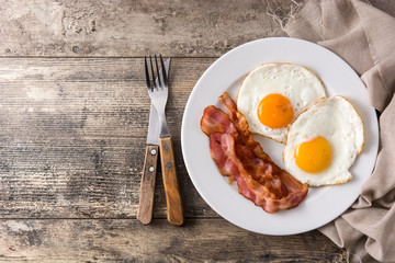 Fried eggs and bacon for breakfast on wooden table. Top view. Copyspace