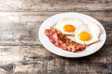 Fried eggs and bacon for breakfast on wooden table. Copyspace