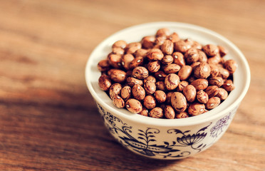 Beans (Phaseolus) in white porcelain bowl on wooden background, vegetarian concept.