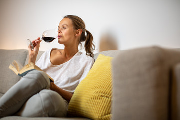 Pretty, young woman drinking some nice red wine at home, in the evening after work on her sofa...