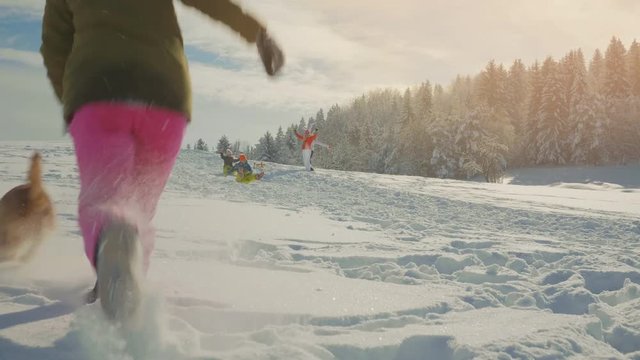 Two Kids Sledding Down A Hill While A Teenager Is Chasing Her Dog