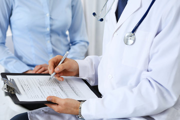 Male doctor holding application form while consulting female patient in hospital. Medicine and healthcare concept