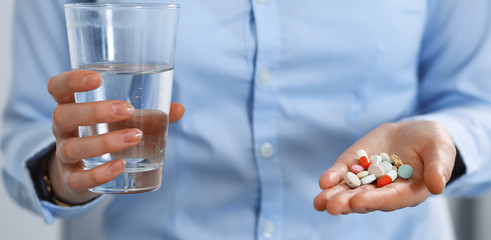 Young unknown woman holding pills and glass of water, closeup of hands.  Medicine and healthcare concept