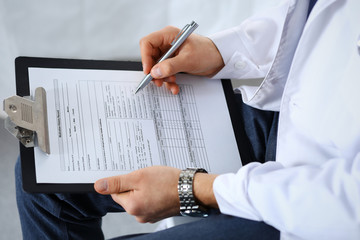 Doctor man filling up medical form on clipboard at hospital, close-up. Healthcare, insurance and medicine concept 