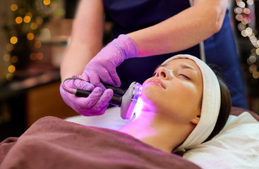 people, beauty, cosmetic treatment, cosmetology and technology concept - beautician with microdermabrasion device doing face exfoliation to young woman lying at spa