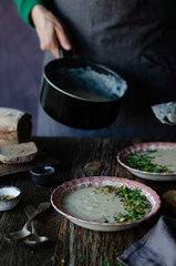Woman is filling up bowls with fresh vegetable soup in the kitchen.