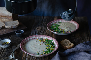 The man is filling up bowls with fresh vegetable soup in the kitchen.