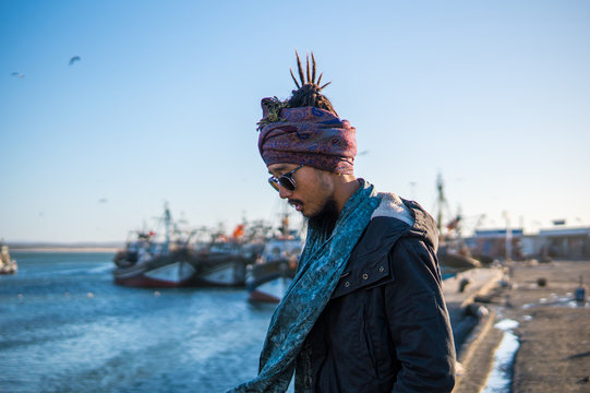 Young Asian Bearded Tourist man with Dreadlocks and scarf on head Walking on the Ocean Coast in Essaouira, Morocco at the evening sunset time