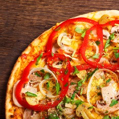Top view close up Italian pizza with melted cheese, red tomatoes, pepper, mushrooms, onion and herbs on a brown table