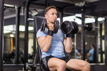 Muscular man doing exercise with dumbbell at the gym.