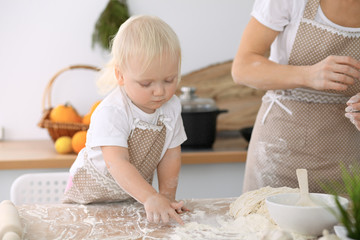 Little girl and her blonde mom in beige aprons  playing and laughing while kneading the dough in kitchen. Homemade pastry for bread, pizza or bake cookies. Family fun and cooking concept