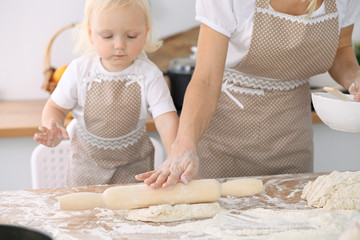 Little girl and her blonde mom in beige aprons  playing and laughing while kneading the dough in kitchen. Homemade pastry for bread, pizza or bake cookies. Family fun and cooking concept