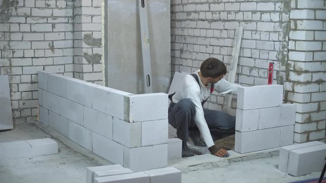construction worker checking evenness of aerated concrete wall with bubble level