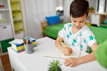 education, childhood and school concept - happy little boy sitting at desk and writing or drawing...