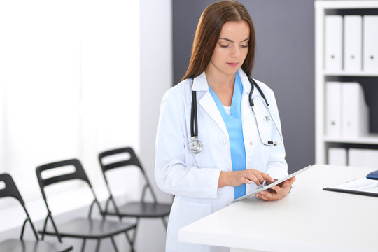 Doctor Woman At Work. Portrait Of Female Physician Using Digital Tablet  While Standing Near Reception Desk At Clinic Or Emergency Hospital. Medicine And Healthcare Concept