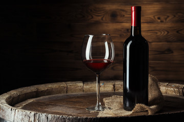 Bottle and glass of red wine on wooden barrel shot with dark wooden background