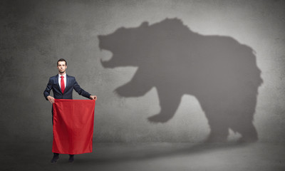Businessman standing with red cloth in his hand and big bear shadow on his background
