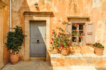 Fototapeta na wymiar Yellow wall of the monastery with doors, window and flowerpots